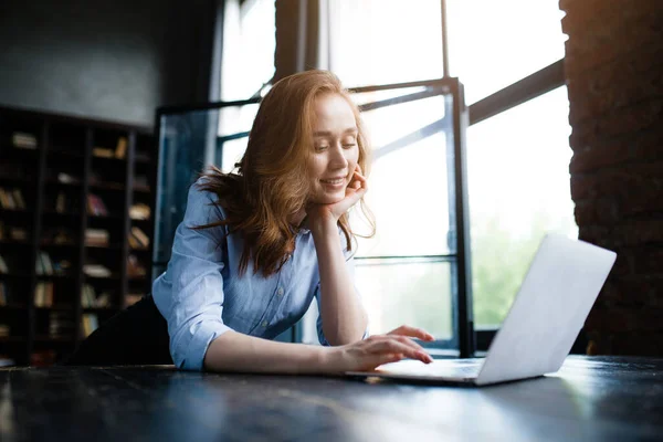 Redhead businesswoman dát bradu na ruce a vypadá pěkně na obrazovce notebooku, zatímco dělá svou práci. — Stock fotografie