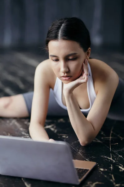 A Thai girl sits on the floor in transverse twine. Blocks his head on his hand and turns on the laptop for online training