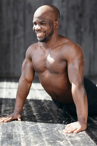 Trener Pilates o ciemnej skórze pochyla się w kręgosłupie, kładąc ręce na drewnianej podłodze na poddaszu.. — Zdjęcie stockowe
