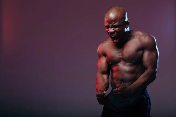 Profesionální boxer s tmavou pletí demonstruje svaly svého trupu a rozpláče válku na neonově červeném pozadí. — Stock fotografie