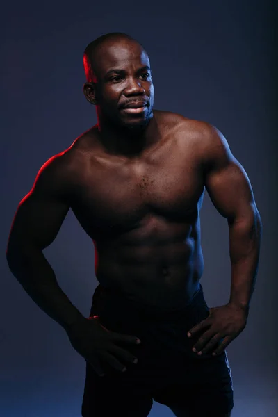 Hombre guapo de piel oscura posando en neón rojo-azul y mostrando músculos de un torso desnudo — Foto de Stock