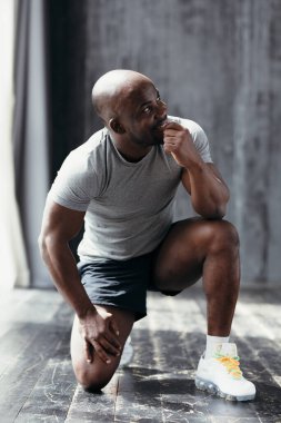 Gri tişörtlü ve siyah şortlu, elini ağzında tutarak çömelmiş bir Afro-Amerikan 'ın profil görüntüsü.