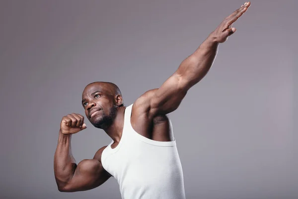 Retrato Muscular culturista masculino en camiseta blanca y pantalones cortos deportivos demuestra sus músculos estirando el brazo en el estudio — Foto de Stock