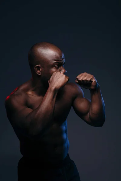 Tmavý boxer trénuje s nahým trupem. Sportovec s reliéfními svaly je podsvícen modrým světlem. — Stock fotografie