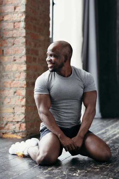 Yakışıklı, kaslı, Afrikalı bir Amerikalının portresi. Spor salonunda dizlerinin üzerine çöküp pencereden dışarı bakıyor..