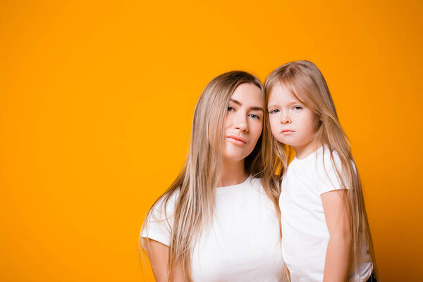 Mom and daughter are not happy that they are sitting on self-isolation. Portrait of a family on an orange background