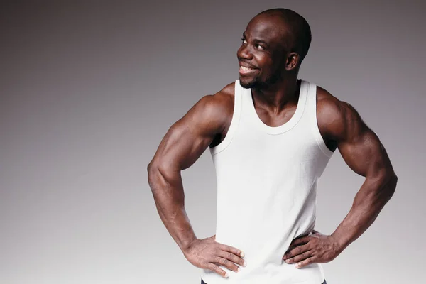 Homem americano africano muscular em t-shirt branca em pé sobre fundo cinza e sorrindo. Homem com uma profissão de modelo — Fotografia de Stock