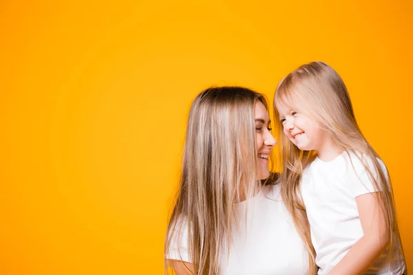 Mom and daughter hug each other and smile on an orange background. Happy family relationships — Stock Photo, Image
