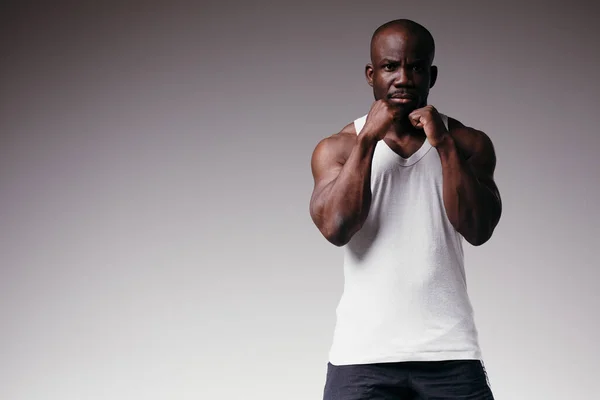 Homem treinador de fitness com músculos em relevo em uma camiseta branca fica em um fundo cinza. Demonstração um estilo de vida saudável — Fotografia de Stock