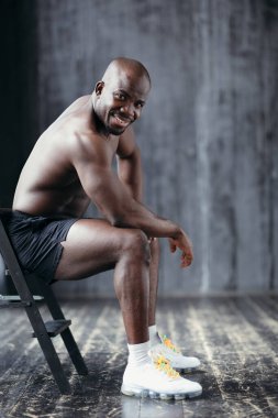 Çekici üstsüz Afrikalı Amerikalı bir sandalyede oturuyor ve kolunda pazılar ve pazılar gösteriyor.