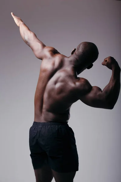 Boxerův zadní pohled. Svalnatá záda černocha. Sportovec demonstruje biceps a zvedne jednu ruku — Stock fotografie