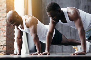 Beyaz tişörtlü siyah bir koç öğrencisine spor salonunda doğru şınav çekmeyi öğretir..