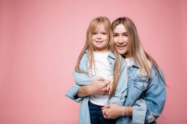 Uzun saçlı anne ve kızı pembe arka planda birbirlerine sıkıca sarılıyorlar. Mutlu ebeveyn-çocuk ilişkisi