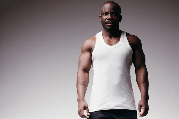 Hermoso culturista negro en una camiseta blanca muestra músculos.Hombre fuerte con abdominales, hombros, bíceps, tríceps y pecho perfectos — Foto de Stock