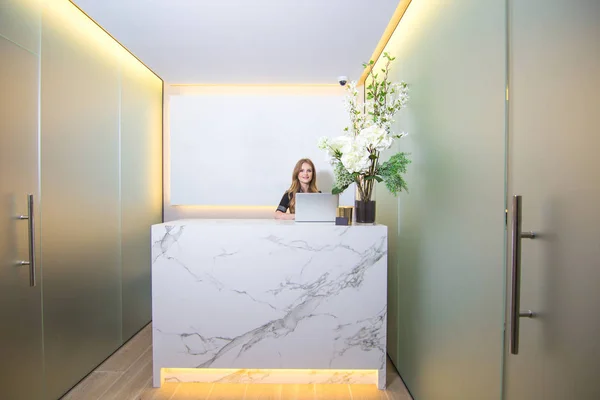 Tezgahın arkasında güzel ve gülümseyen bir kadın olan modern bir kliniğin resepsiyonu..