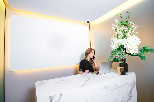 Genç ve güzel bir resepsiyonist telefonda konuşuyor. Arkaplanda kopyalama alanı olan boş ekran.