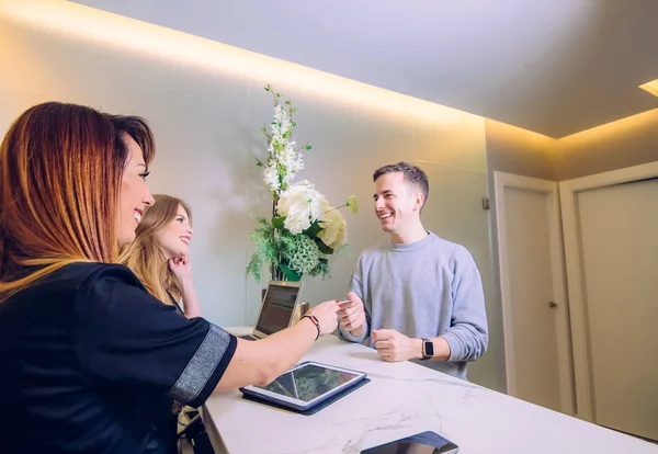 Üniformalı, gülümseyen genç bayan resepsiyonistler güzellik salonundaki mutlu müşterilere katılıyorlar..