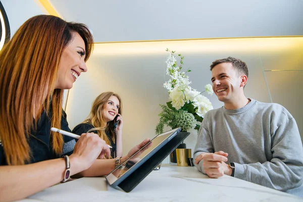 Kliniğin modern resepsiyonunda bir hastaya bakan kadın resepsiyonistler. Randevu almak için tablet ve telefon kullanıyorlar..