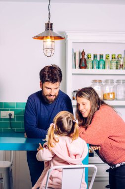 Mutfak masasında oturan küçük kızlarına bakan mutlu anne ve baba. Aile evde..