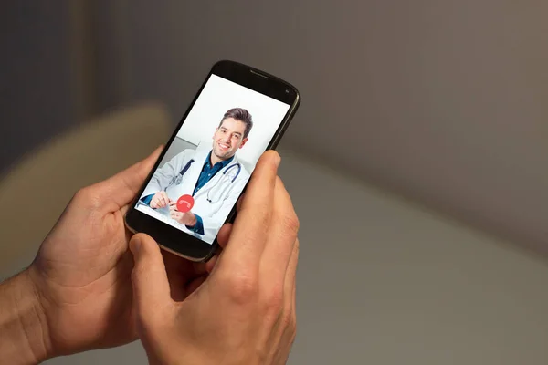 Video conference with doctor at home. Man hands holding smartphone with doctor video call on the screen