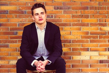 Genç iş adamı tuğla duvarlı arka planda dışarıda oturuyor.