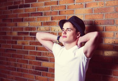 Mutlu ve memnun genç adam ve tuğla duvar arka planı. Ellerini başının arkasına koy..