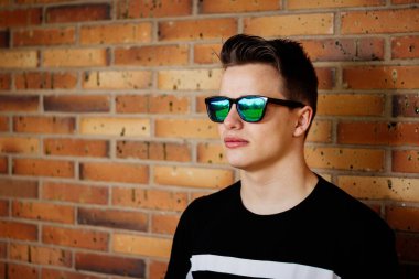 Tuğla duvara karşı güneş gözlüklü genç adam