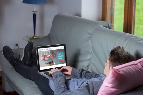 Młody Człowiek Leżący Kanapie Podczas Korzystania Laptopa Wideo Opieki Zdrowotnej — Zdjęcie stockowe