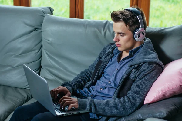 Kulaklıklı genç adam evde dizüstü bilgisayar kullanıyor.