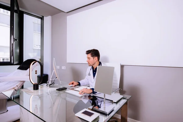 Modern tıp ofisinde çalışan steteskoplu yakışıklı genç bir doktor.