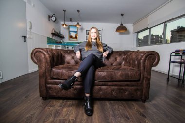 Modern bir dairede televizyon izlerken koltukta oturan kendinden emin ve rahat genç bir kadının portresi..