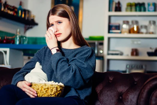 Evdeki oturma odasındaki kanepede oturup televizyon izlerken ağlayan üzgün bir genç..