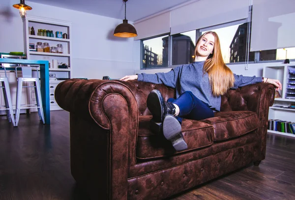 Evdeki kanepede oturan ve kameraya bakan genç bir kadın..