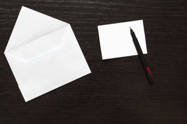 Boş beyaz bir zarf ve tahta bir masanın arka planında bir kalem olan bir kağıt.