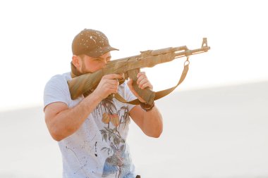 Kızgın adam çöl şapkası bandana kurukafa tişörtü Kalaşnikov silah makineli tüfek gün batımı beyaz kum Barkhan