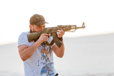 Kızgın adam çöl şapkası bandana kurukafa tişörtü Kalaşnikov silah makineli tüfek gün batımı beyaz kum Barkhan