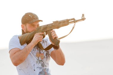 Kızgın adam çöl şapkası bandana kurukafa tişörtü Kalaşnikov silah makineli tüfek gün batımı beyaz kum Barkhan