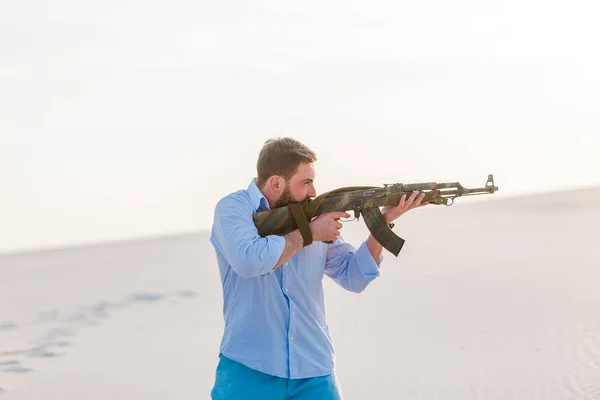 man standing bracelet desert shirt blue pans kalashnikov weapon machine-gun sunset white sand barkhan