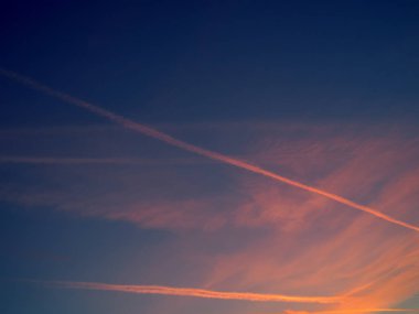 Mavi gökyüzünde gün batımı ve uçak izleri.