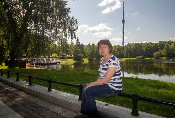 Gölün arka planında ve Moskova 'daki Ostankino kulesinde çitlerin üzerinde oturan bir kadın.