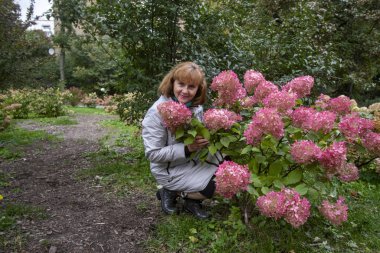 Beyaz yağmurluklu Rus kadın parktaki renge oturdu.