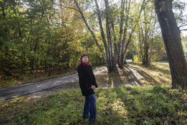 Sonbahar. Parktaki çalıların ve ağaçların arka planında kırmızı yakalı siyah ceketli bayan Kuskovo.
