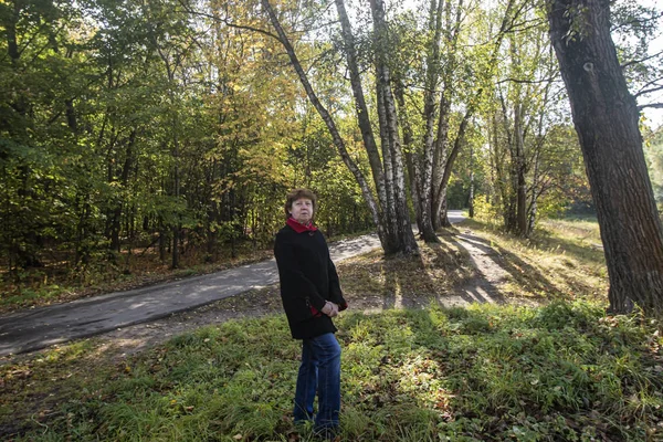 Sonbahar. Parktaki çalıların ve ağaçların arka planında kırmızı yakalı siyah ceketli bayan Kuskovo.