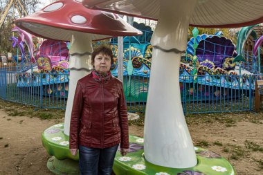 Sonbahar. Kırmızı deri ceketli ve kotlu bir kadın. Dekoratif büyük mantarların yanında..