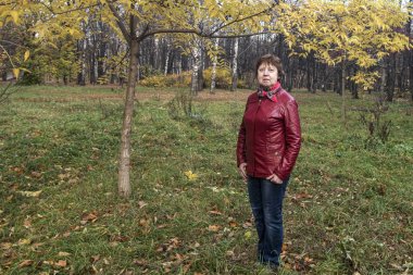  Sonbahar. Kırmızı deri ceketli bir bayan sarı dağ kül yapraklarının arkasında duruyor.