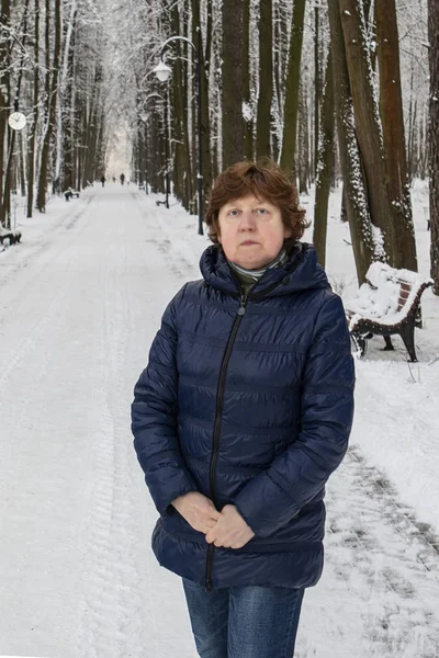 Kış. Mavi spor ceketli bir bayan karlı bir ormanda dar bir sokakta duruyor.