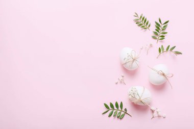 Çiçekli beyaz Paskalya yumurtaları ve pembe arka planda yeşil yapraklar.