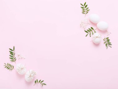 Çiçekli beyaz Paskalya yumurtaları ve pembe arka planda yeşil yapraklar.