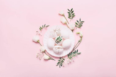 Çiçekli beyaz Paskalya yumurtaları ve pembe arka planda yeşil yapraklar.