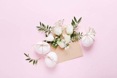 Beyaz Paskalya yumurtaları ve pembe arka planda çiçekli ve yeşil yapraklı zarf.
